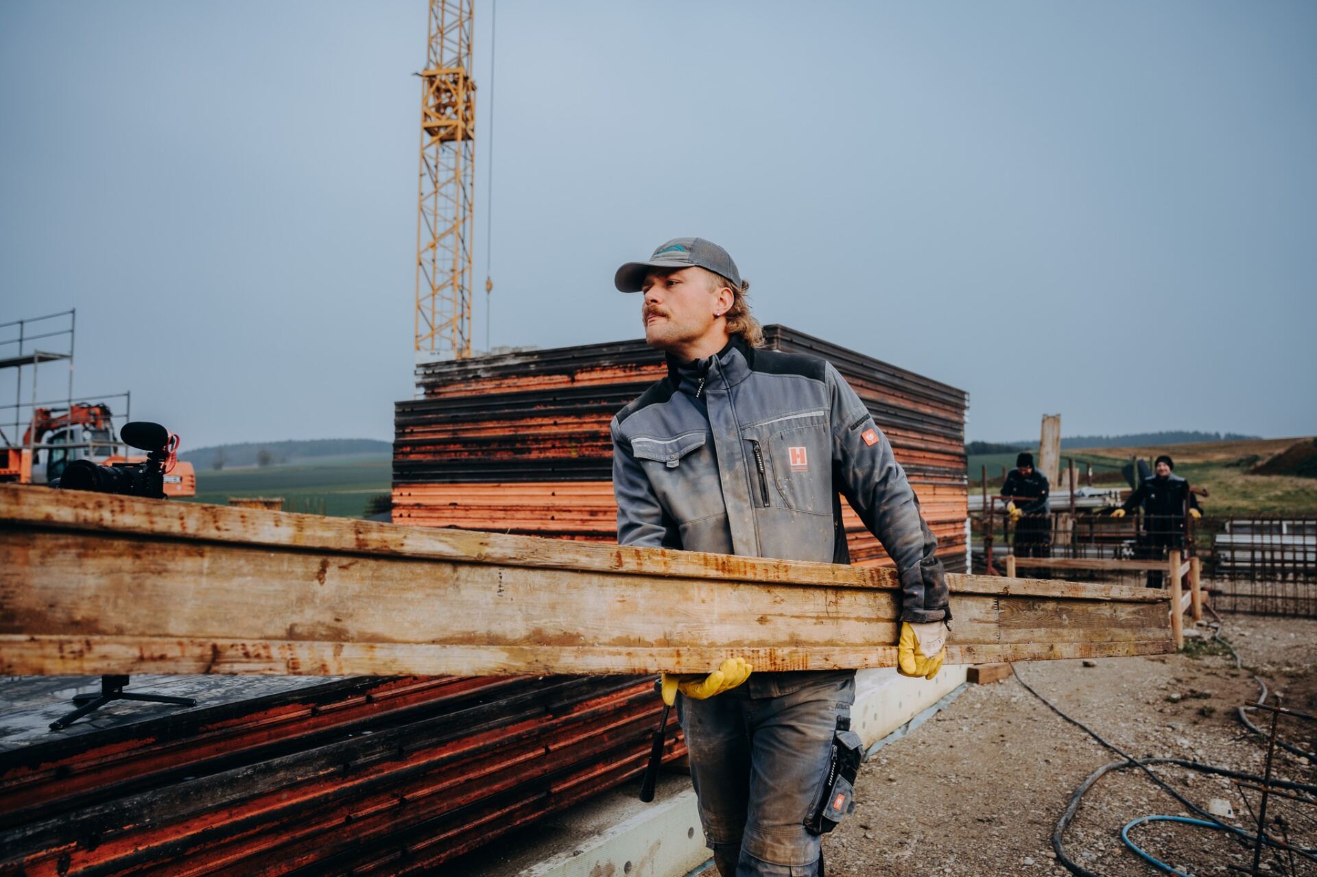 Krojer Bau – Holzbalken vor Baukran tragen