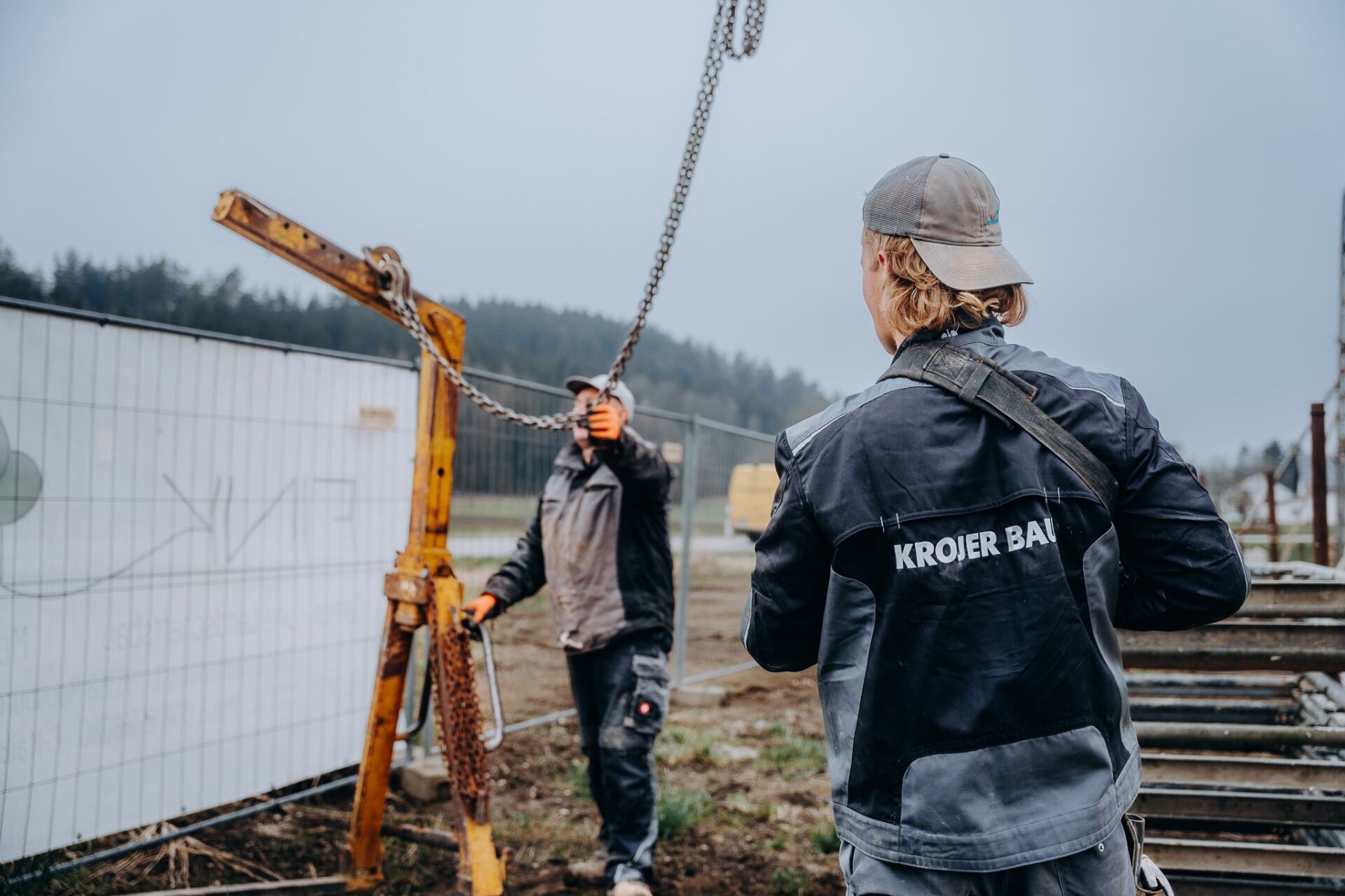 Krojer Bau – Zwei Krojer Bau Mitarbeiter koordinieren Kranarbeit mit Kette