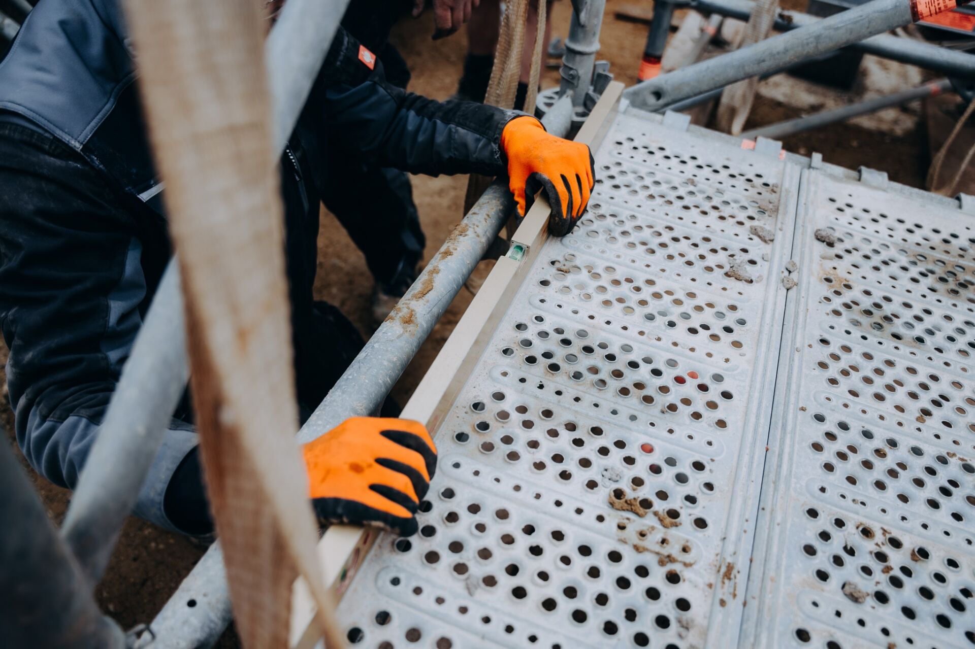 Krojer Bau – Nivellieren am Gerüst mit orangenen Handschuhen